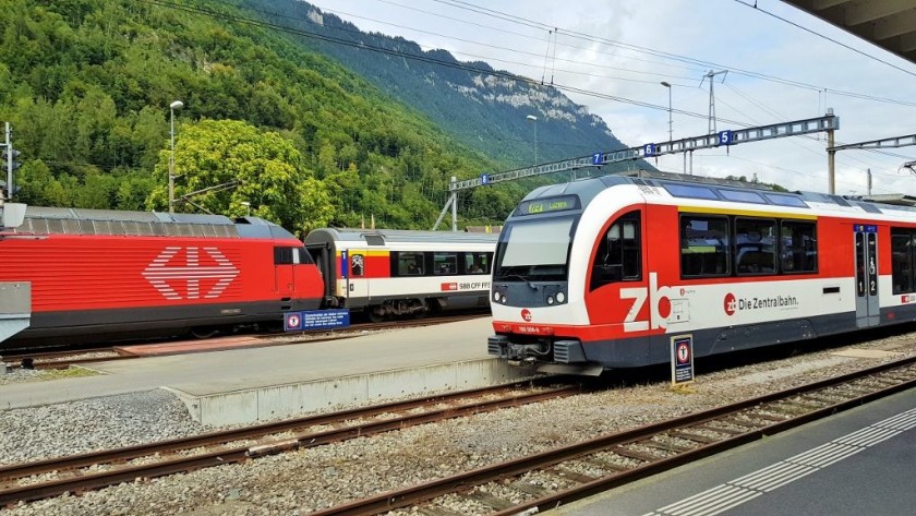 An IC train departs on the left behind a Luzern - Interlaken Express